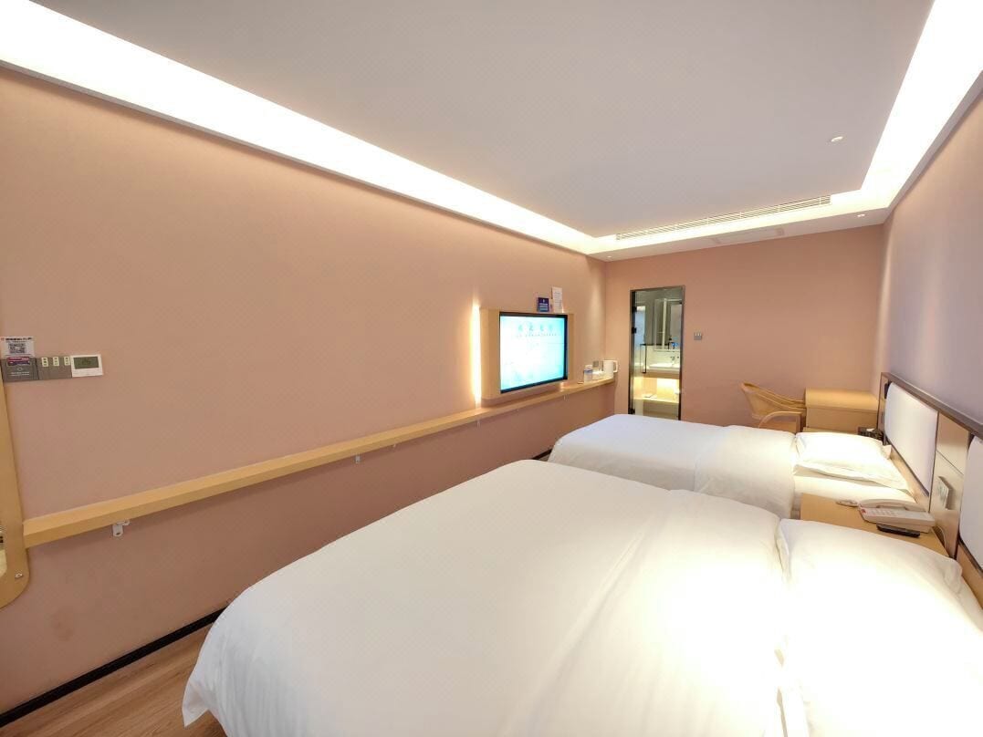 A hotel room with two beds, a television on the wall, and a small desk with a chair.