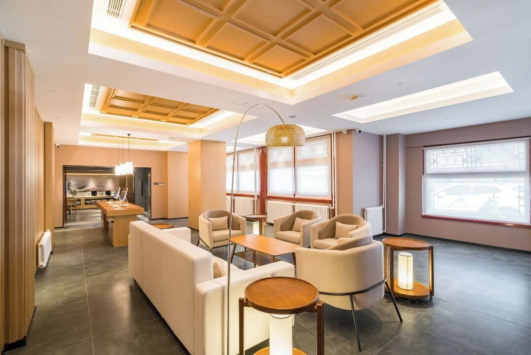 A modern hotel lobby with a seating area, a kitchen in the background, and large windows providing natural light.