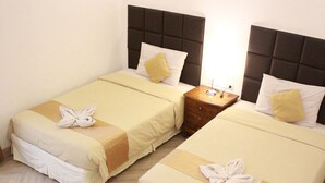 Two twin beds with matching headboards, a bedside table with a lamp, and a neatly made bed with a towel. - Salak Boutique Hotel (Bogor)