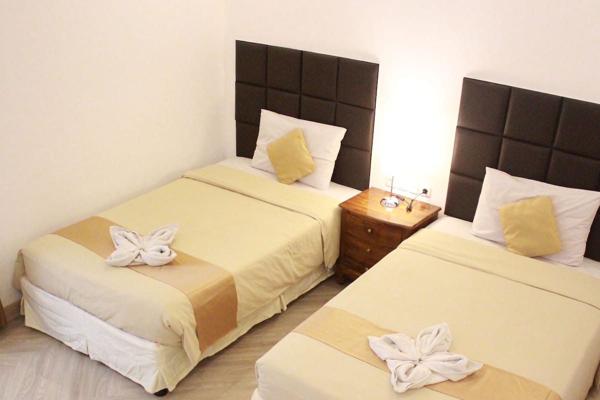 Two twin beds with matching headboards, a bedside table with a lamp, and a neatly made bed with a towel.