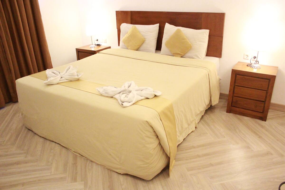 A hotel room with a large bed, two bedside tables, and a wooden headboard.