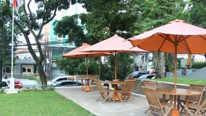 An outdoor seating area with wooden tables and chairs, surrounded by orange umbrellas. - Salak Boutique Hotel (Bogor)