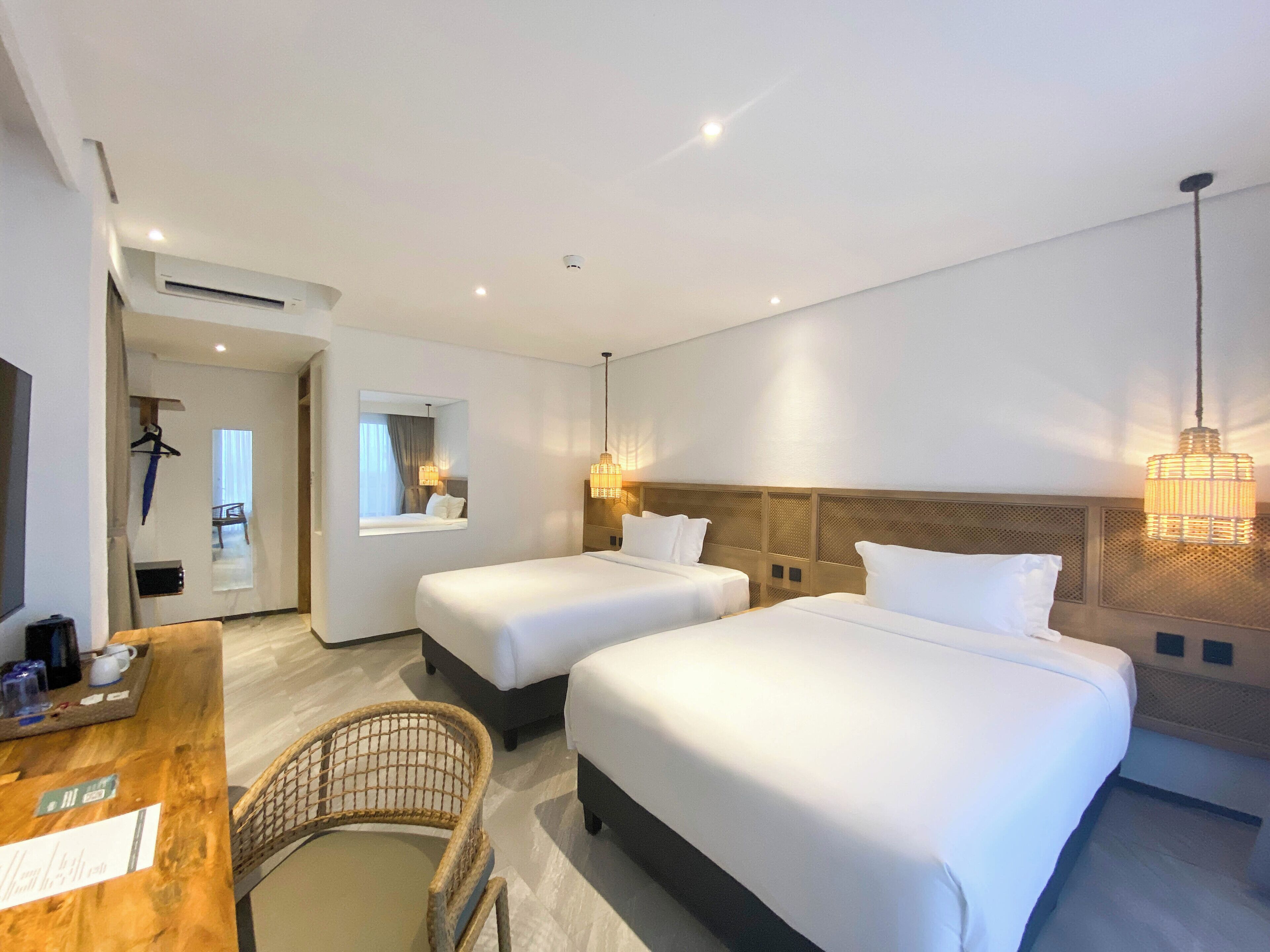 A hotel room with two beds, a wooden desk, a chair, and a mirror.