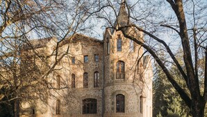 A stone building with arched windows and a tower, surrounded by trees and tables set for dining. - Castell de Villavecchia - Castle with pool Girona Barcelona (Sant Hilari Sacalm)