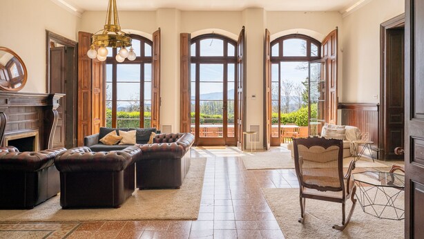 A spacious living room with a fireplace, leather sofas, a dining area, and large windows with a view. - Castell de Villavecchia - Castle with pool Girona Barcelona (Sant Hilari Sacalm)