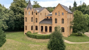A large, historic stone building with multiple towers and arched windows, surrounded by well-maintained lawns and trees. - Castell de Villavecchia - Castle with pool Girona Barcelona (Sant Hilari Sacalm)