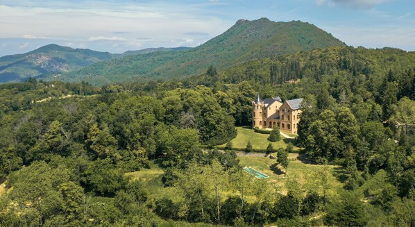 Un edificio grande e histórico rodeado de un bosque denso y montañas.