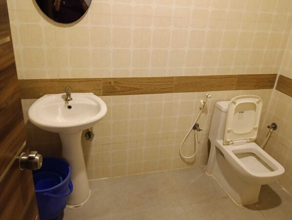 A bathroom with a sink, toilet, and bidet. There is a blue trash bin and a mirror above the sink. - RR Residency (Mysore)