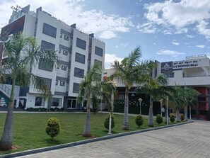 A modern building with multiple floors, a paved walkway, and palm trees. - RR Residency (Mysore)