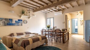Ein gemütliches Wohnzimmer mit einer Couch, einem Esstisch mit Stühlen, einem blauen Teppich und einer Küchenzeile mit Kühlschrank.