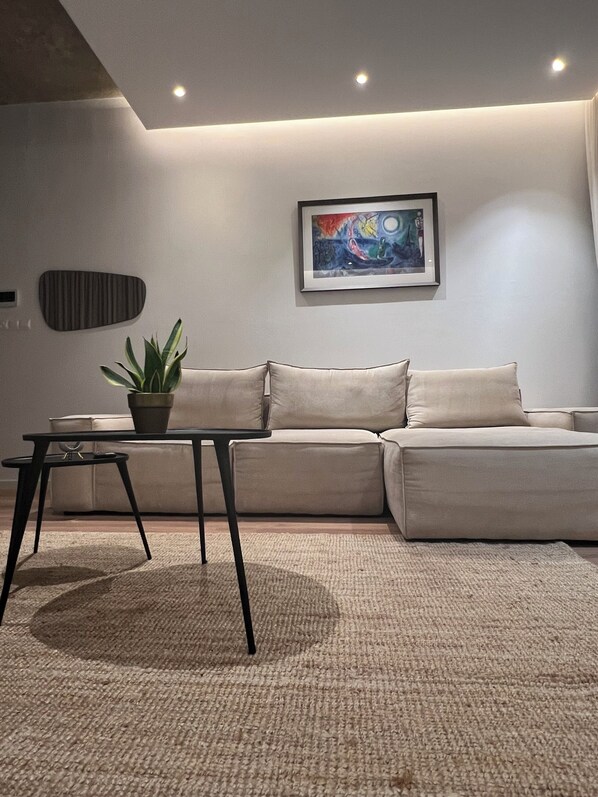 Una sala de estar moderna con un sofá beige, una mesita negra con una planta y un cuadro abstracto enmarcado en la pared.