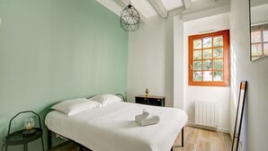Un dormitorio con cama, una silla, una mesita de noche, un ventanal y un radiador.