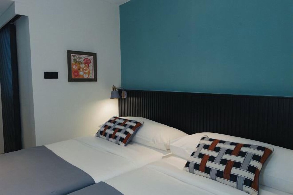 Una cama doble con cabecera, dos almohadas y una mesita de noche con lámpara.