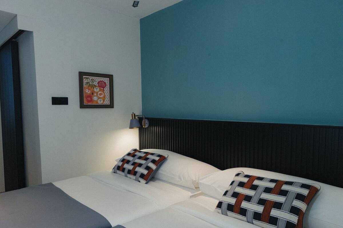 Ein Hotelzimmer mit einem Bett, zwei Kissen, einem Nachttisch, einer Lampe und einem gerahmten Bild an der Wand.