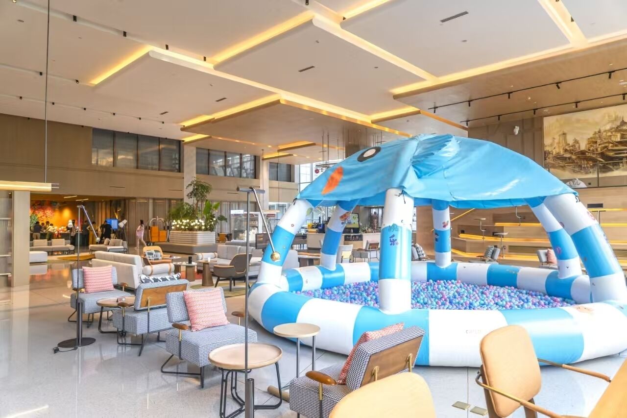 A modern lobby with a blue and white inflatable play area, comfortable seating, and a large window offering a view of the city.