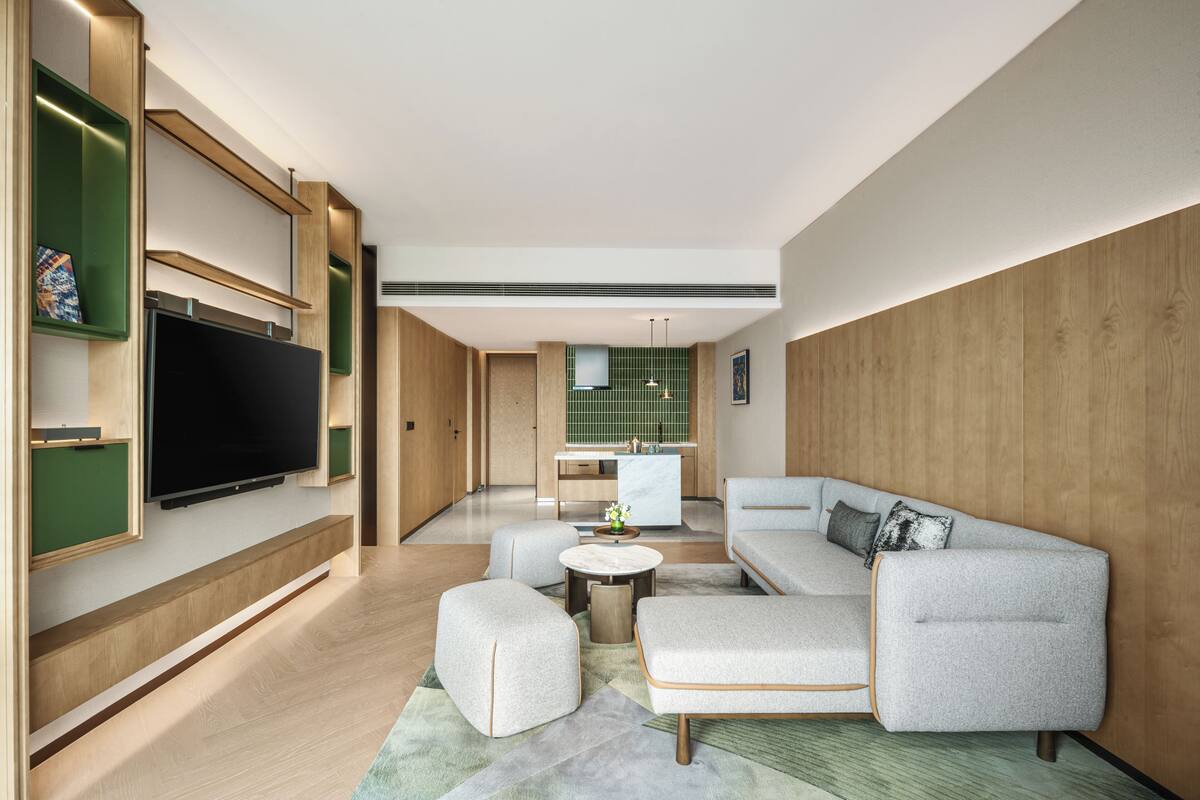 Una sala moderna con un televisor de pantalla plana, un sofá modular, una mesa de centro y una cocina al fondo.