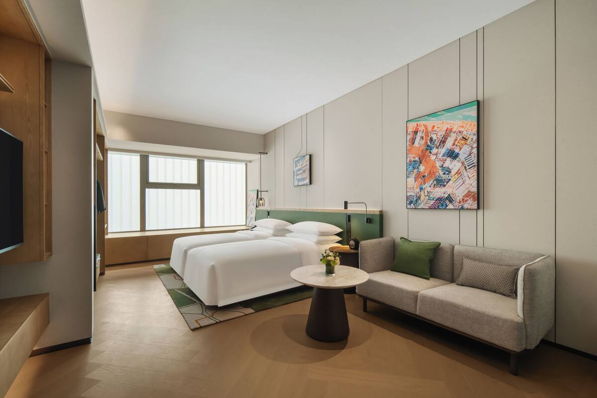 Una habitación de hotel moderna con una cama, un sofá, una mesita de centro y un ventanal grande.
