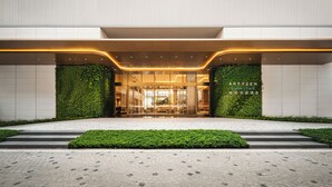 Une entrée d'hôtel moderne avec des portes en verre, une haie verte et un chemin pavé.