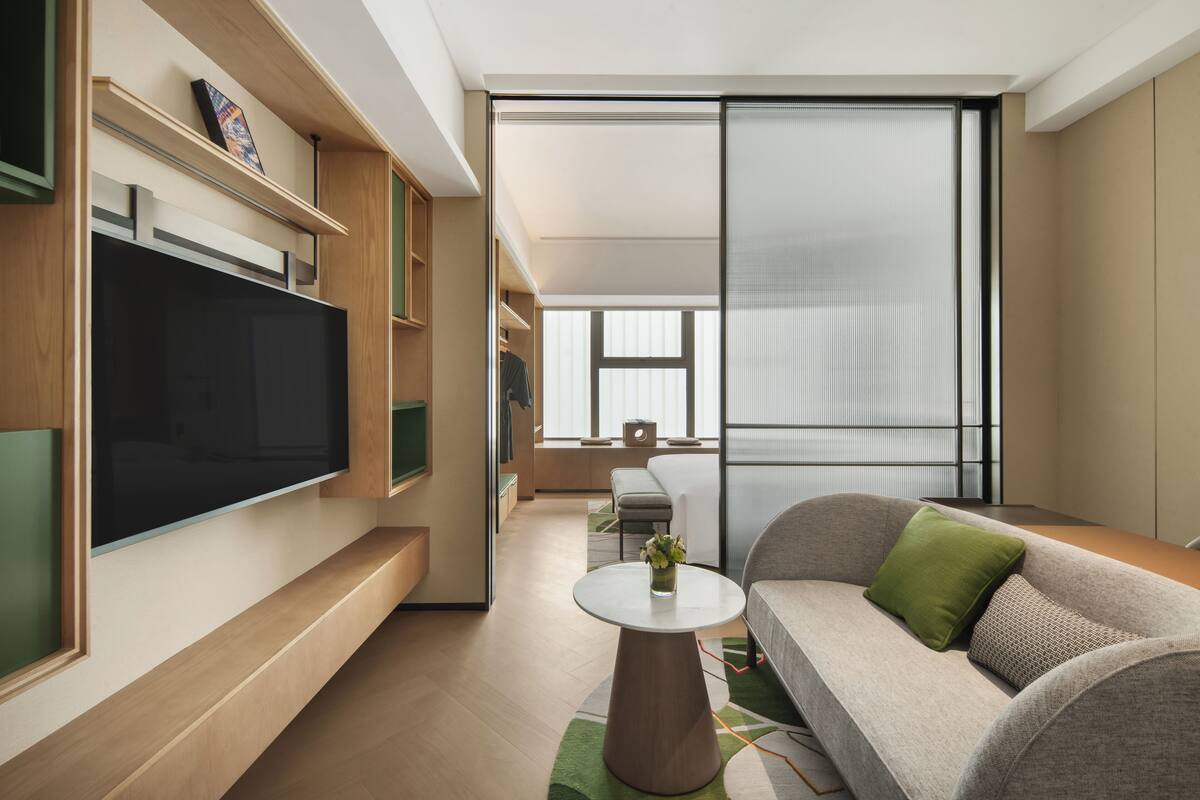 Una sala de estar moderna con un televisor de pantalla plana, un sofá con cojines verdes, una mesa de centro redonda y un gran ventanal corredero que da a un balcón.