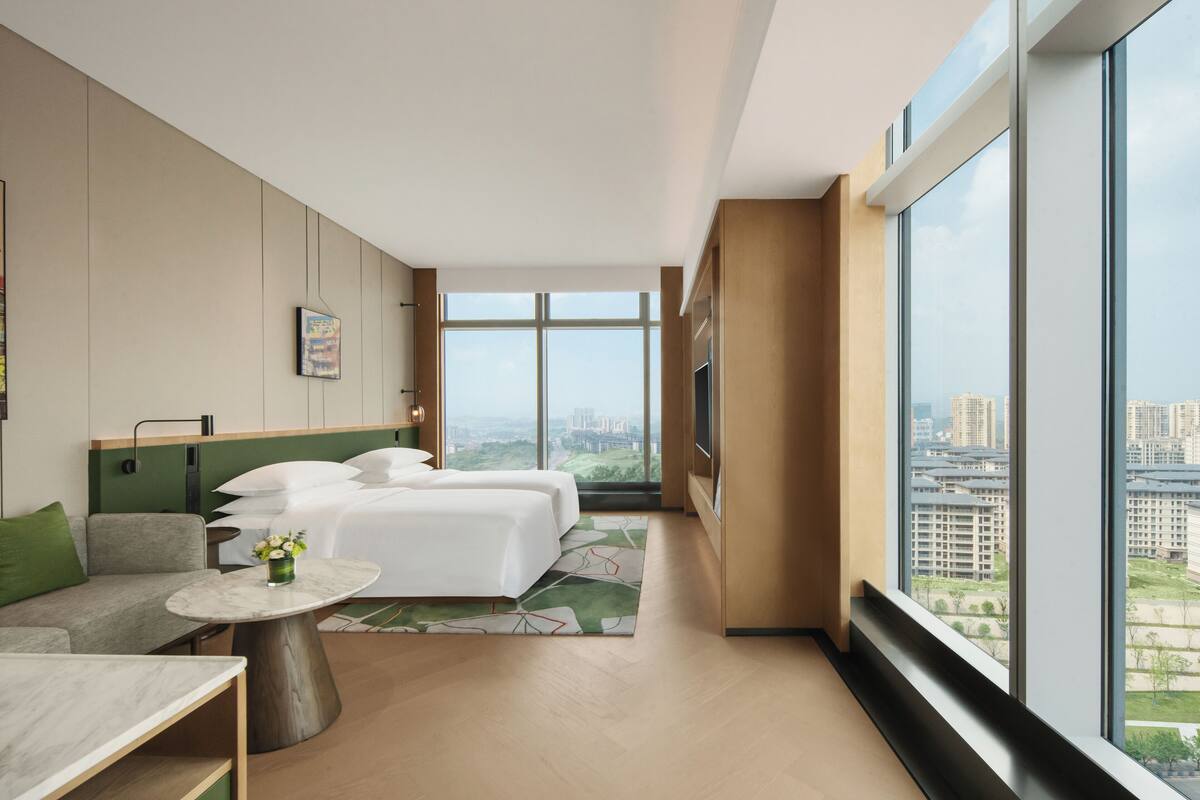 Una habitación de hotel moderna con un ventanal grande, una cama, un sofá y una mesita.