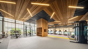 Une salle de sport avec des panneaux de plafond en bois, du matériel d’exercice et de grandes fenêtres.