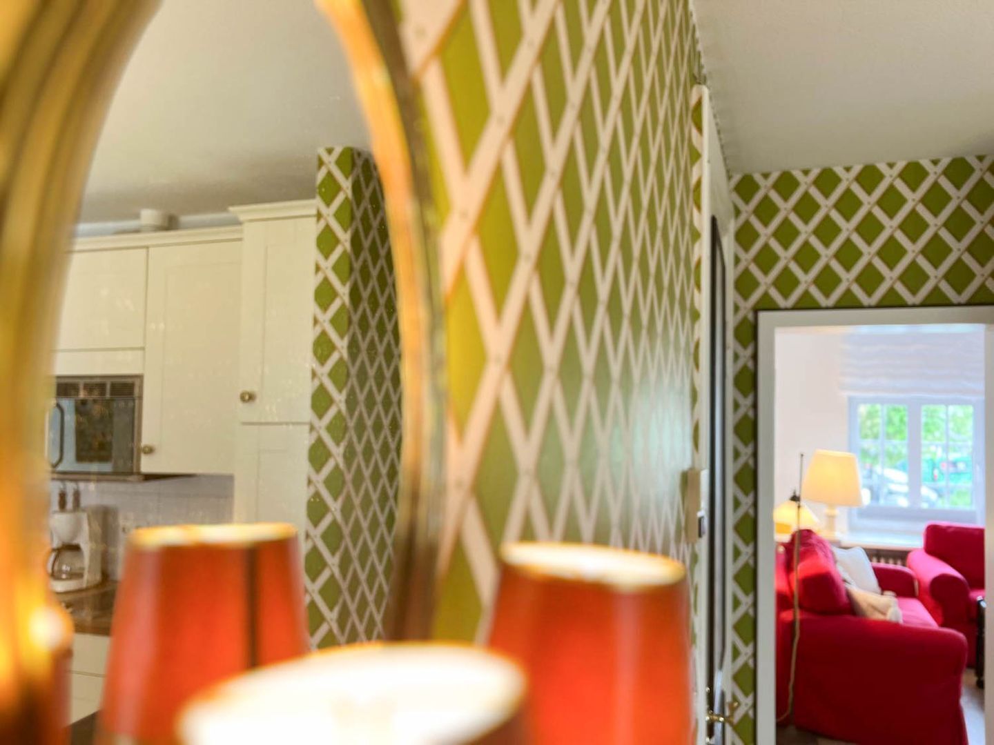 A room with a green and white patterned wall, a red sofa, and a kitchen area in the background.