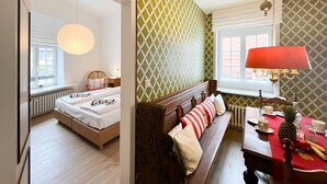 A room with a bed, a wooden bench with cushions, a table with a red tablecloth, and a hanging lamp. - House Friesland - Apartment 1 - An urban villa with spacious and tasteful (Sylt)