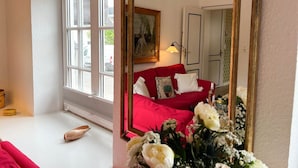 A room with a red sofa, a painting on the wall, a window with blinds, and a mirror reflecting the room. - House Friesland - Apartment 1 - An urban villa with spacious and tasteful (Sylt)