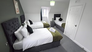 Une chambre moderne avec un grand lit, un lit plus petit, une table de chevet, un bureau et une porte.