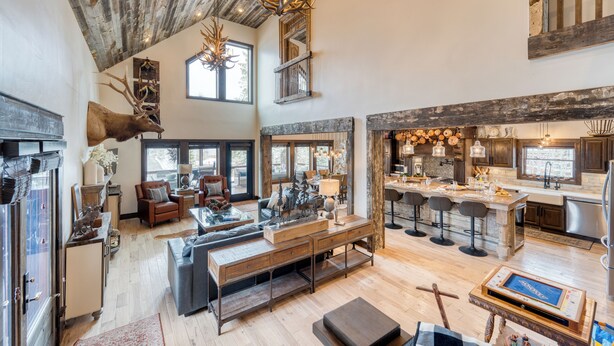 A spacious living area with a high ceiling, rustic decor, a fireplace, and a modern kitchen with bar stools. - Hot Tub, Firepit & Views, Sleeps 19 | Winterhaven Estate by AvantStay (Winter Park)