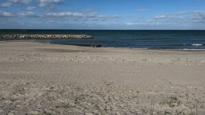 Une plage dotée d’une digue rocheuse, d’un rivage sablonneux et d’une végétation clairsemée.