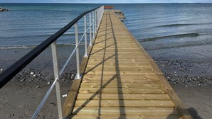 Un muelle de madera que se adentra en el mar, con una barandilla de metal en un lado.