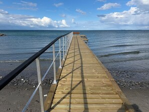 Une jetée en bois s’avançant dans la mer, avec une rambarde métallique d’un côté.