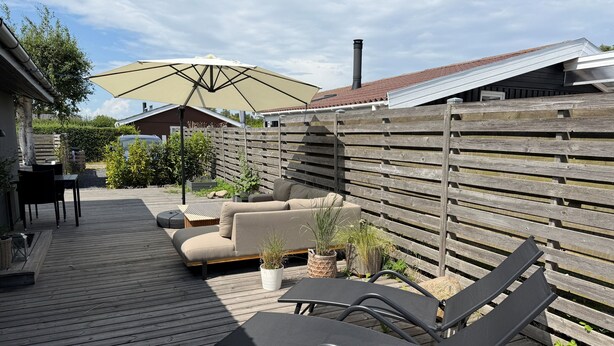 Una terraza de madera con sillones de descanso, una mesa y un paraguas grande.