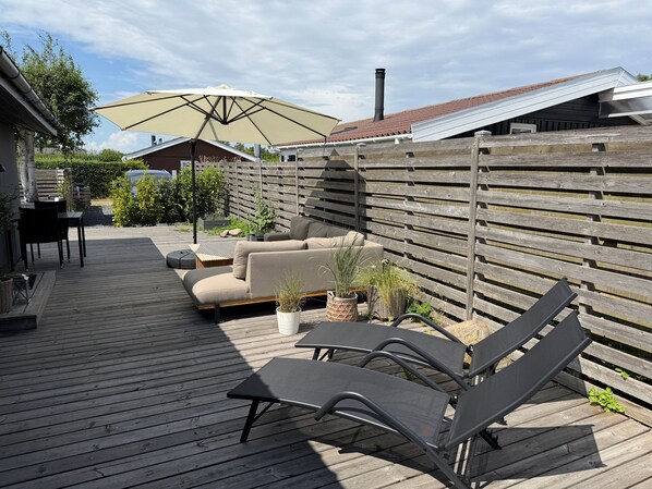 A wooden deck with lounge chairs, a table, and a large umbrella.