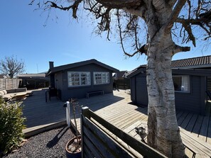 Une terrasse en bois avec un banc, un petit arbre et un bâtiment doté de fenêtres et d’une porte.