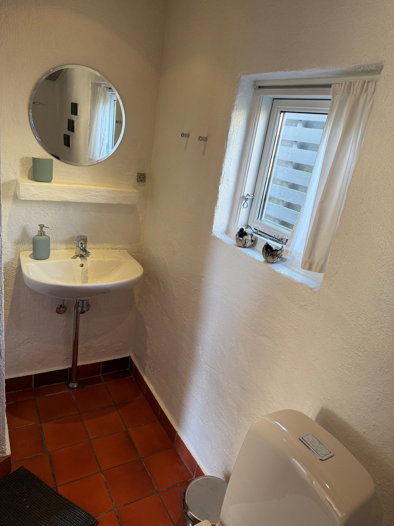 Un baño con lavamanos blanco, un espejo, una ventana con vistas y un inodoro.