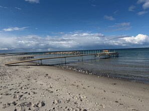 A beach with a wooden pier extending into calm waters, a rocky shoreline, and a clear sky. - Lovely cottage near beautiful bathing beach (Otterup)