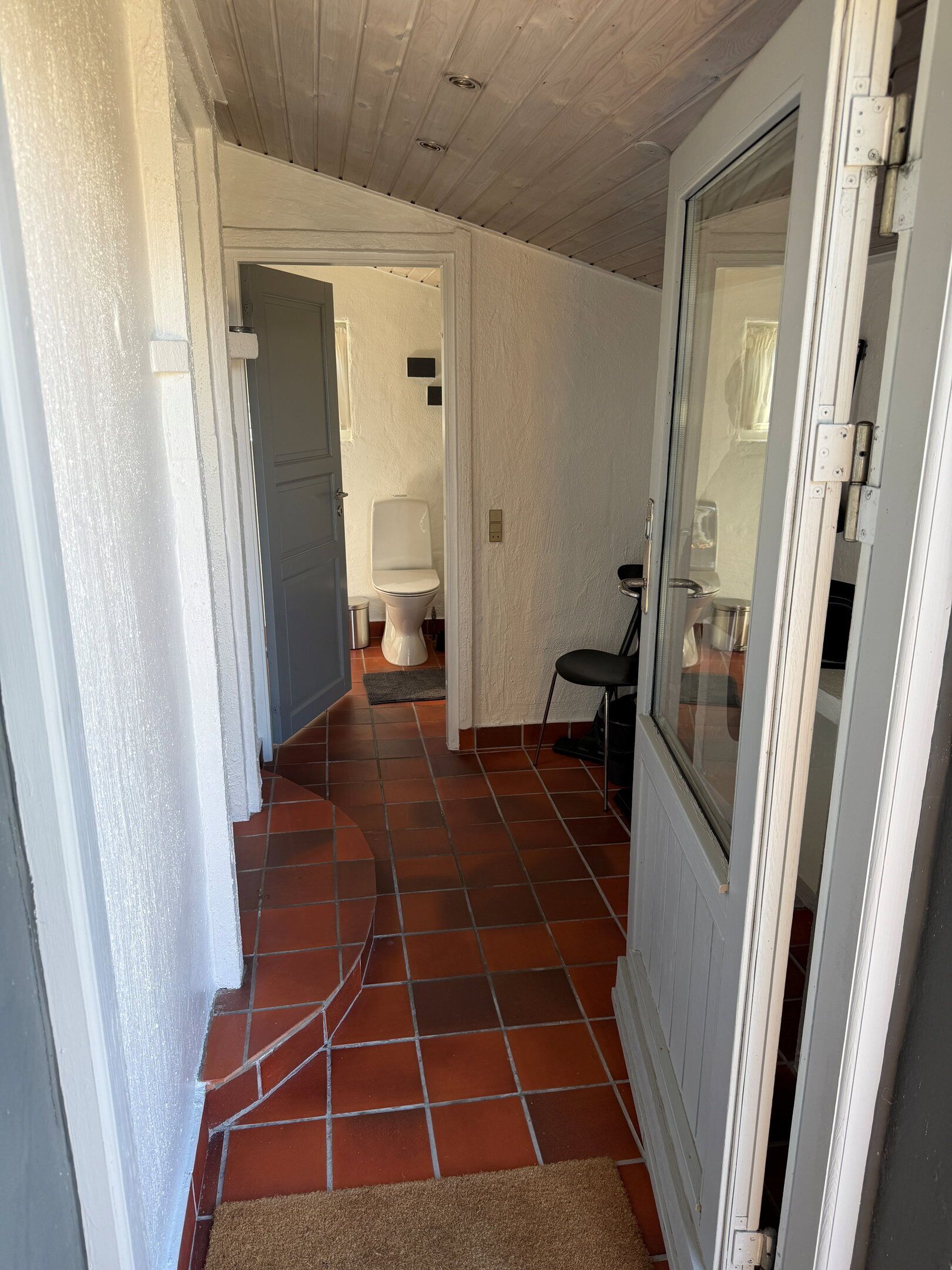 A hallway with a tiled floor, a door, and a view into a bathroom.