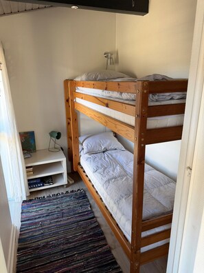 Een stapelbed met een plank eronder, een klein bureau en een kleurrijk vloerkleed.