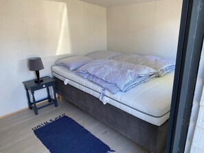 Ein Schlafzimmer mit einem Bett, einem Nachttisch mit Lampe, einem dunkel gefärbten Kopfteil und einem blauen Teppich.