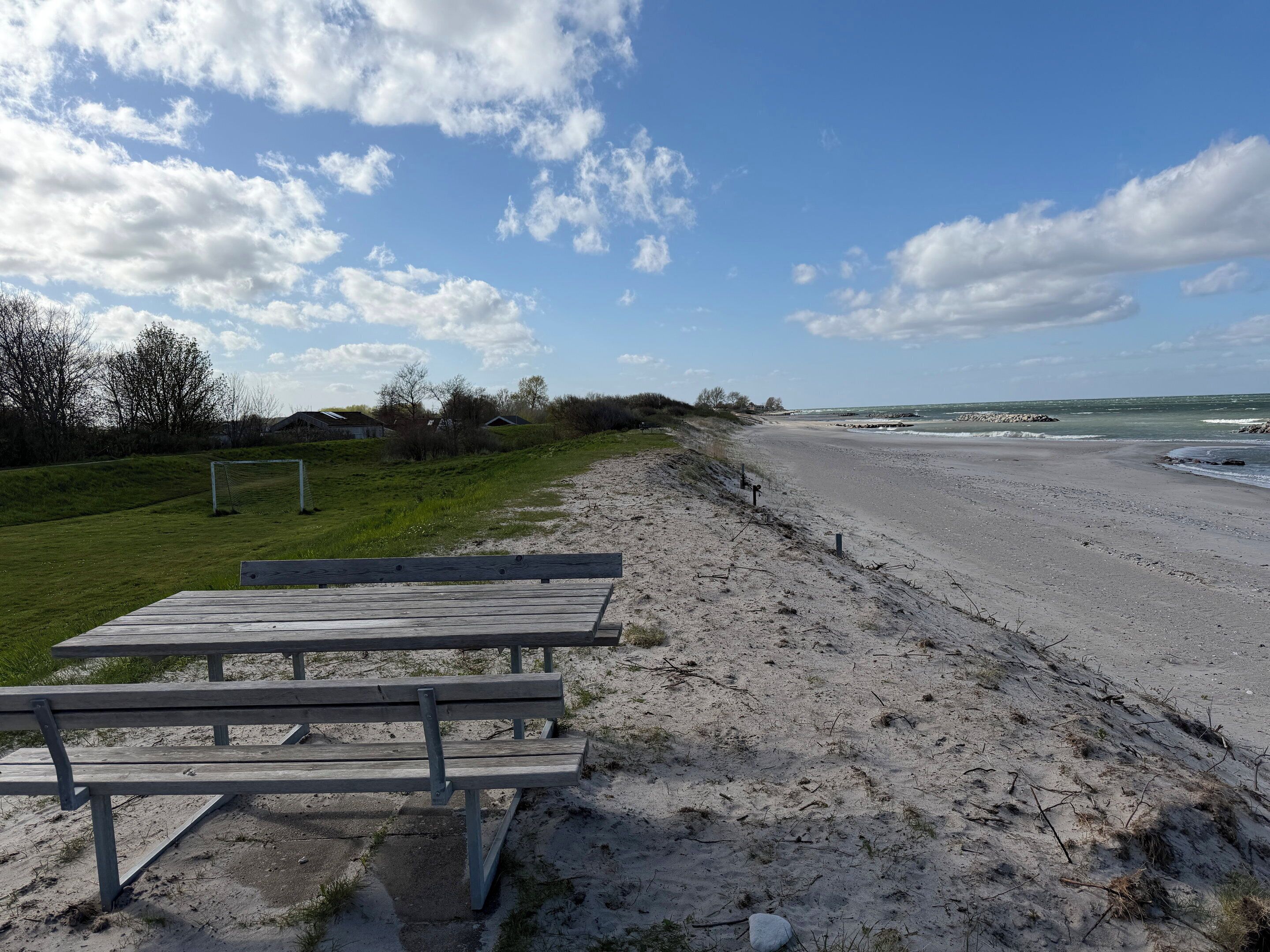 Une plage avec un banc en bois, un but de football et une côte rocheuse.