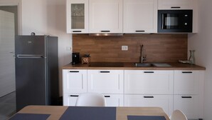 Una cucina moderna con mobili bianchi, un forno a microonde nero e un frigorifero in acciaio inossidabile.