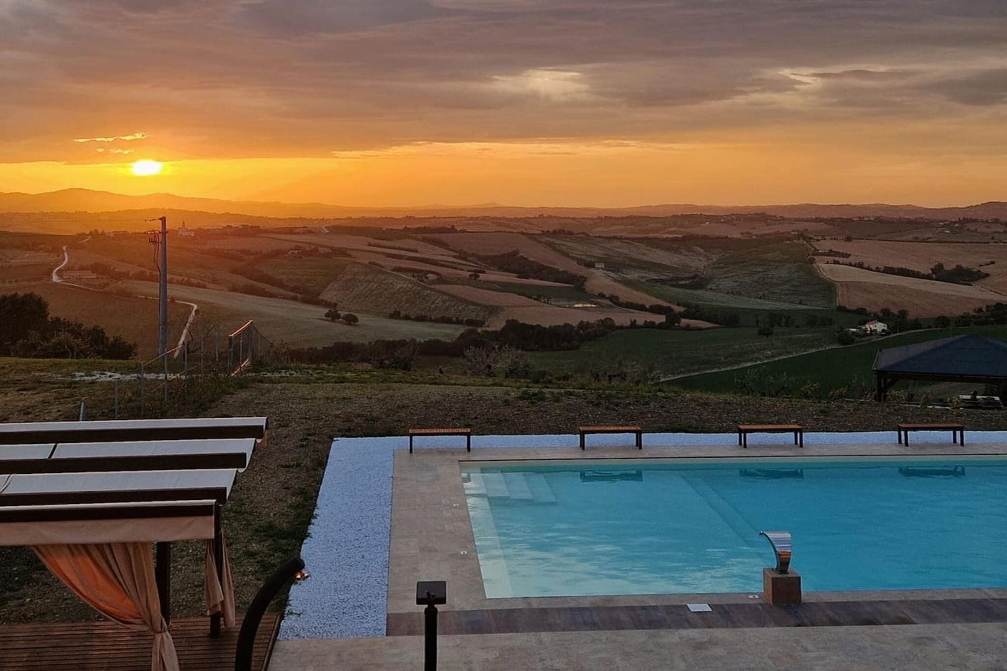 Zwembad met uitzicht op een zonsondergang, omringd door een terras met banken.