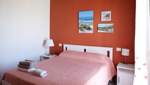 Una camera da letto con un letto, un comodino, una lampada e due quadri appesi raffiguranti scene di spiaggia.