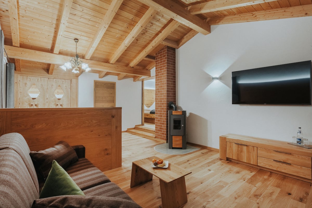 Een moderne woonkamer met houten balken, een open haard, een televisie en een bank.