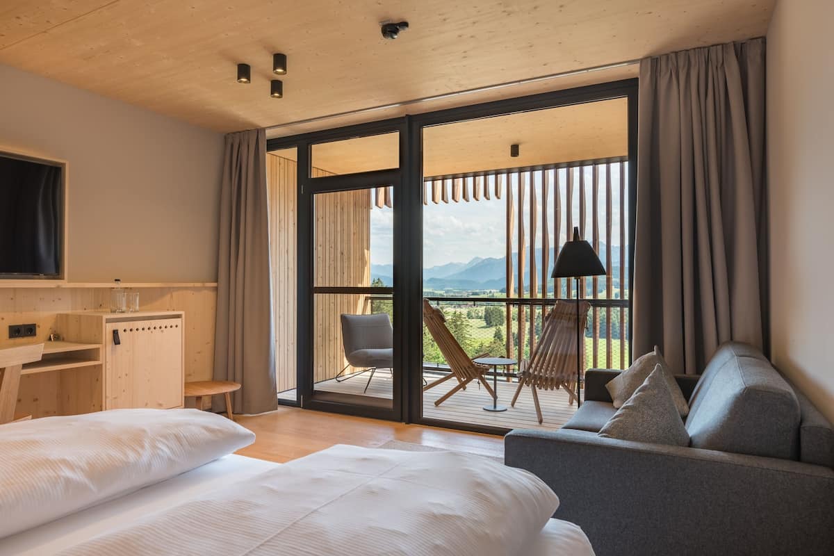 Een moderne hotelkamer met een groot bed, een slaapbank, een bureau en een balkon met uitzicht op de bergen.
