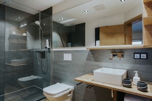 A modern bathroom with a glass-enclosed shower, a wooden vanity with a sink, and a toilet. - Panorama Allgäu Spa Resort (Rueckholz)