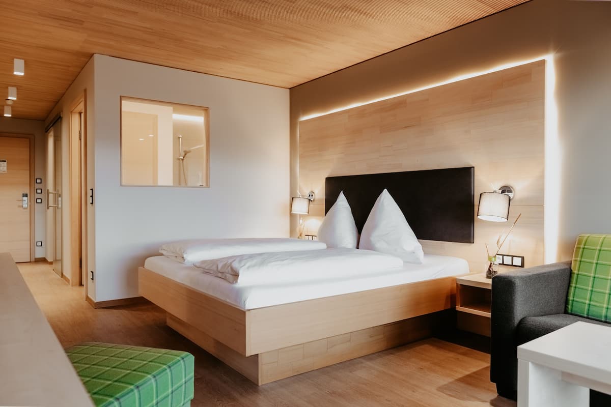 Een moderne hotelkamer met een houten bed, een groene poef, een kleine tafel en een groene stoel.