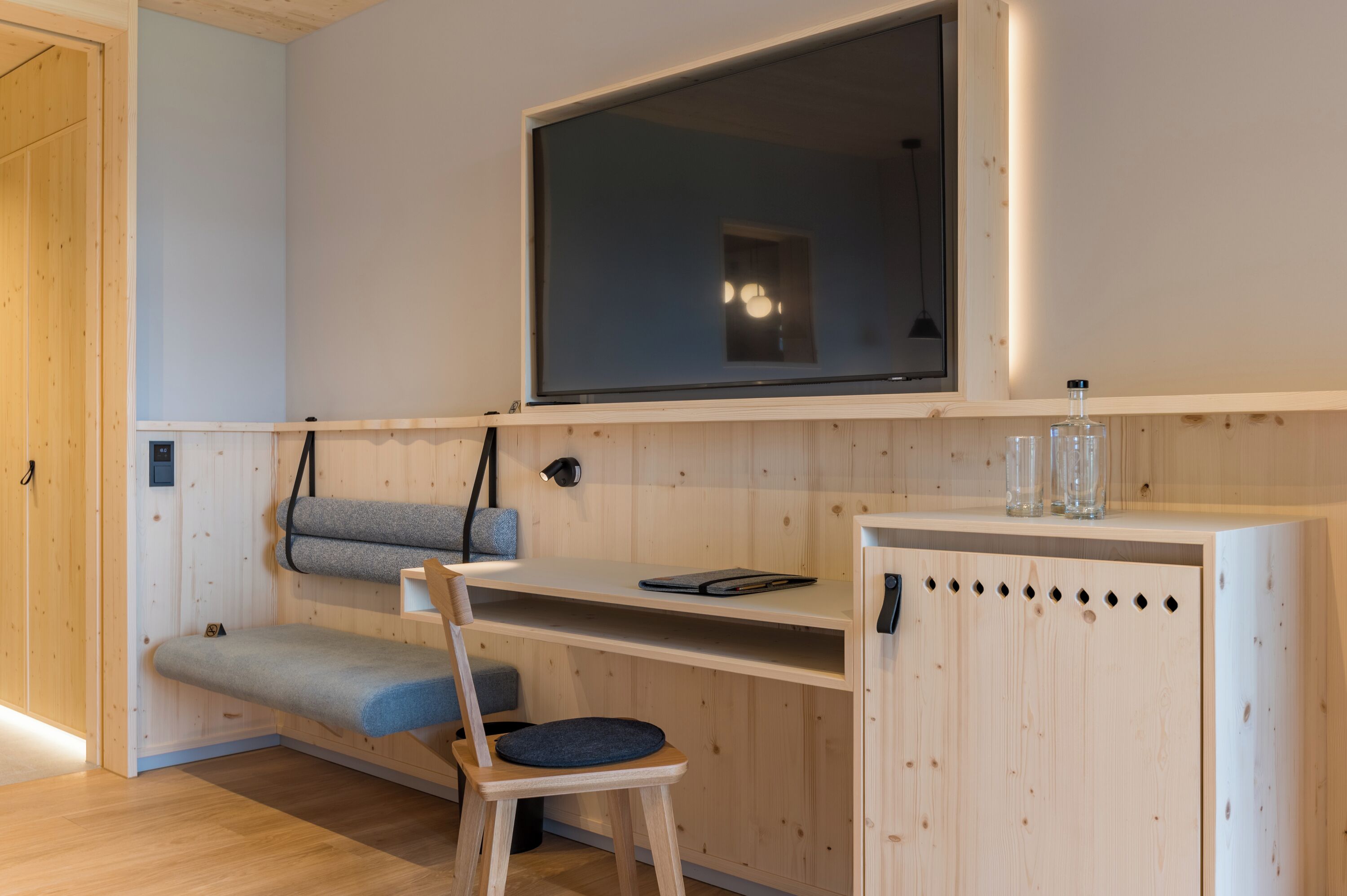 Una habitación con un escritorio de madera, una silla, un ventanal grande y un aparador con cristalería.